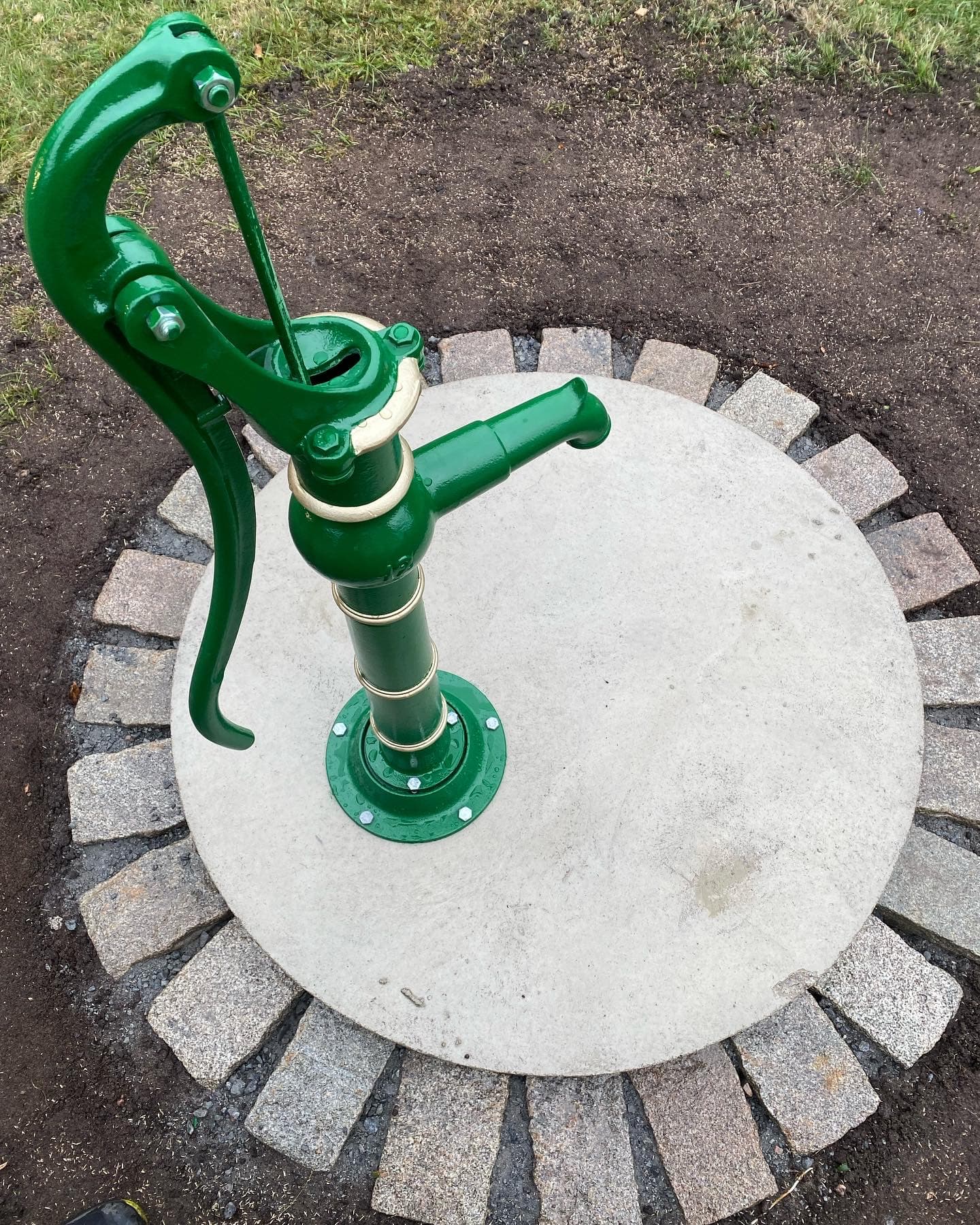 Grön gårdspump installerad på en stensatt yta
